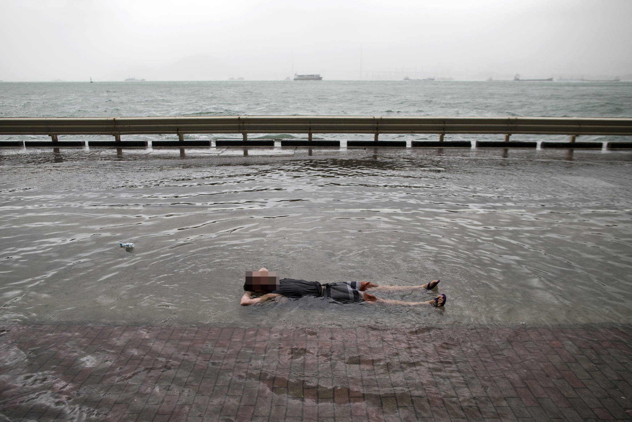 23일 한 홍콩 주민이 제13호 태풍 하토의 영향으로 바닷물이 넘친 빅토리아 항구 도로 위에 누워있다.[EPA=연합뉴스]