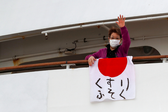 7일 일본 요코하마에 정박 중인 크루즈선 의 한 승객이 ’의약품 부족“이라고 적힌 일본 국기를 발코니에 내건 뒤 손을 흔 드는 모습[로이터=연합뉴스]