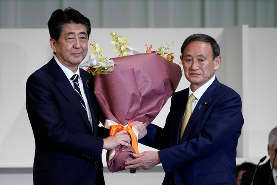 스가 요시히데(오른쪽) 일본 신임 총리가 지난 16일 퇴임하는 아베 신조 전 총리에게 꽃을 건네고 있다. [로이터=연합뉴스]