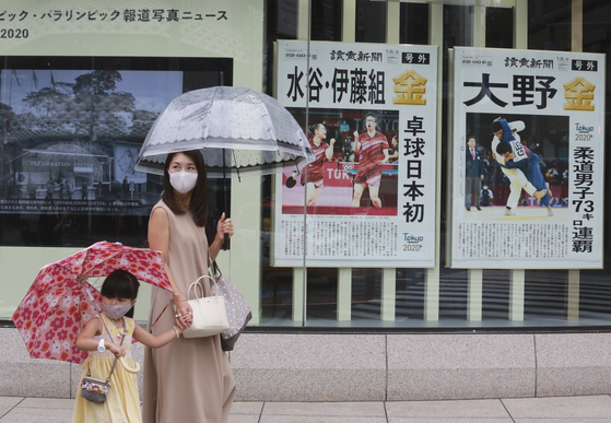 27일 일본 도쿄에서 우산을 쓴 시민들이 올림픽 금메달 소식을 전한 신문 광고판 앞을 지나고 있다. [AP=연합뉴스]