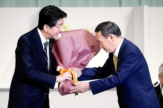 지난해 9월 14일 아베 신조(왼쪽) 당시 일본 총리가 자민당 총재선거에서 승리한 스가 요시히데에게 꽃다발을 건네고 있다. [로이터=연합뉴스]