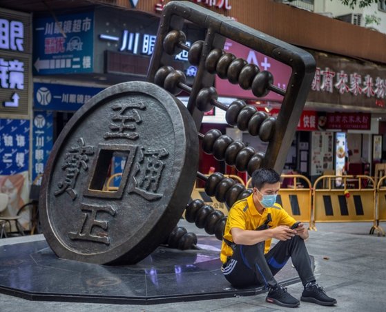 중국 광둥성 광저우의 한 거리에서 한 시민이 마스크를 쓴 채 화폐와 주판 조각상 옆에 앉아 스마트폰을 보고 있다.[EPA=연합뉴스]