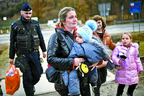 우크라이나와 폴란드 국경 크로스치엔코에 도착한 난민이 폴란드 국경경찰과 이동하고 있다. [AFP=연합뉴스]